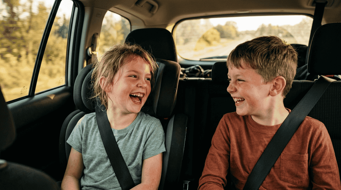 Two children laughing together in the back seat during a family car ride