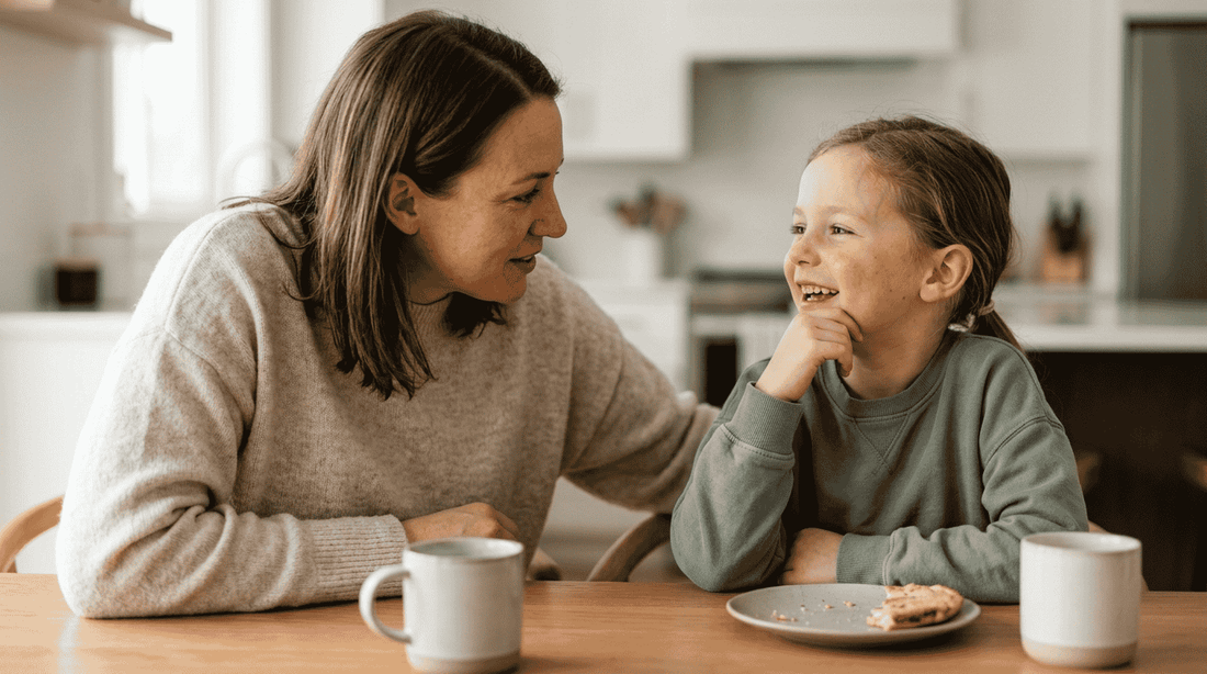 A mother and her young daughter talking and smiling at the kitchen table 