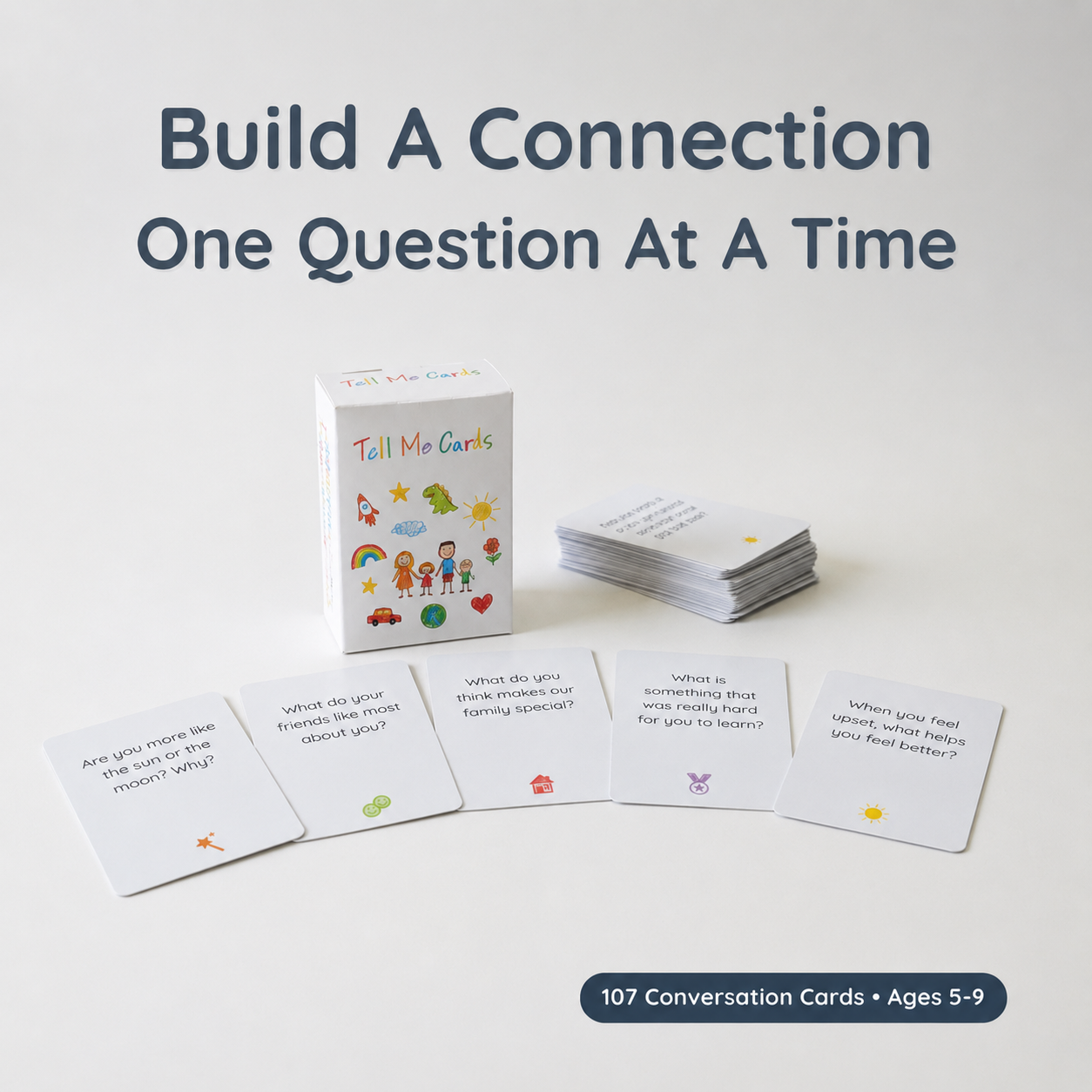 Tell Me Cards conversation card set with a white box, a stack of cards, and five sample cards fanned out on a light gray background. Large text at the top reads 'Build A Connection One Question At A Time' and a badge at the bottom says '107 Conversation Cards • Ages 5-9'.